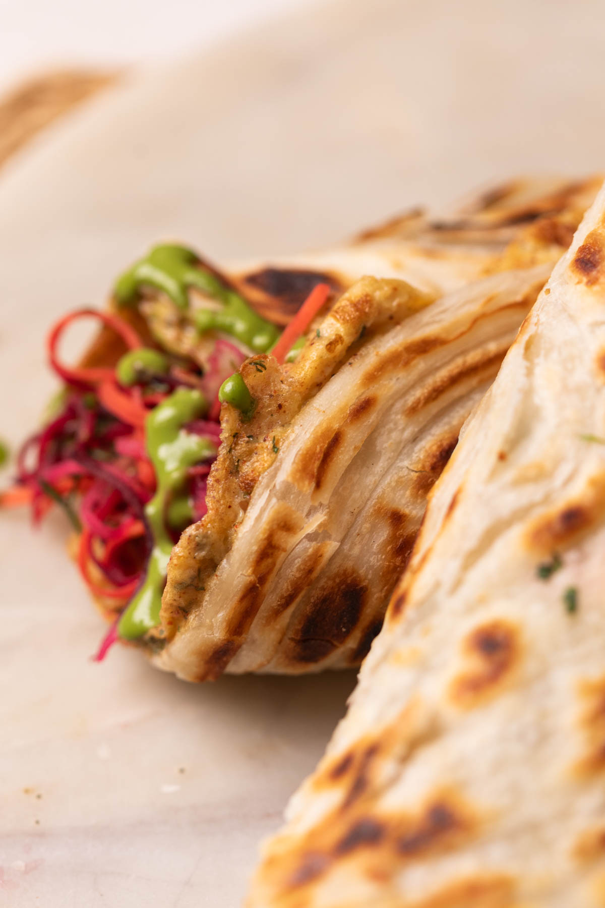 close up image of rolled up anda paratha to show its flaky texture and filling