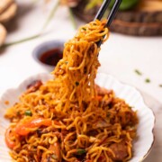 an image of chilli chicken noodles picked up with a pair of chopsticks