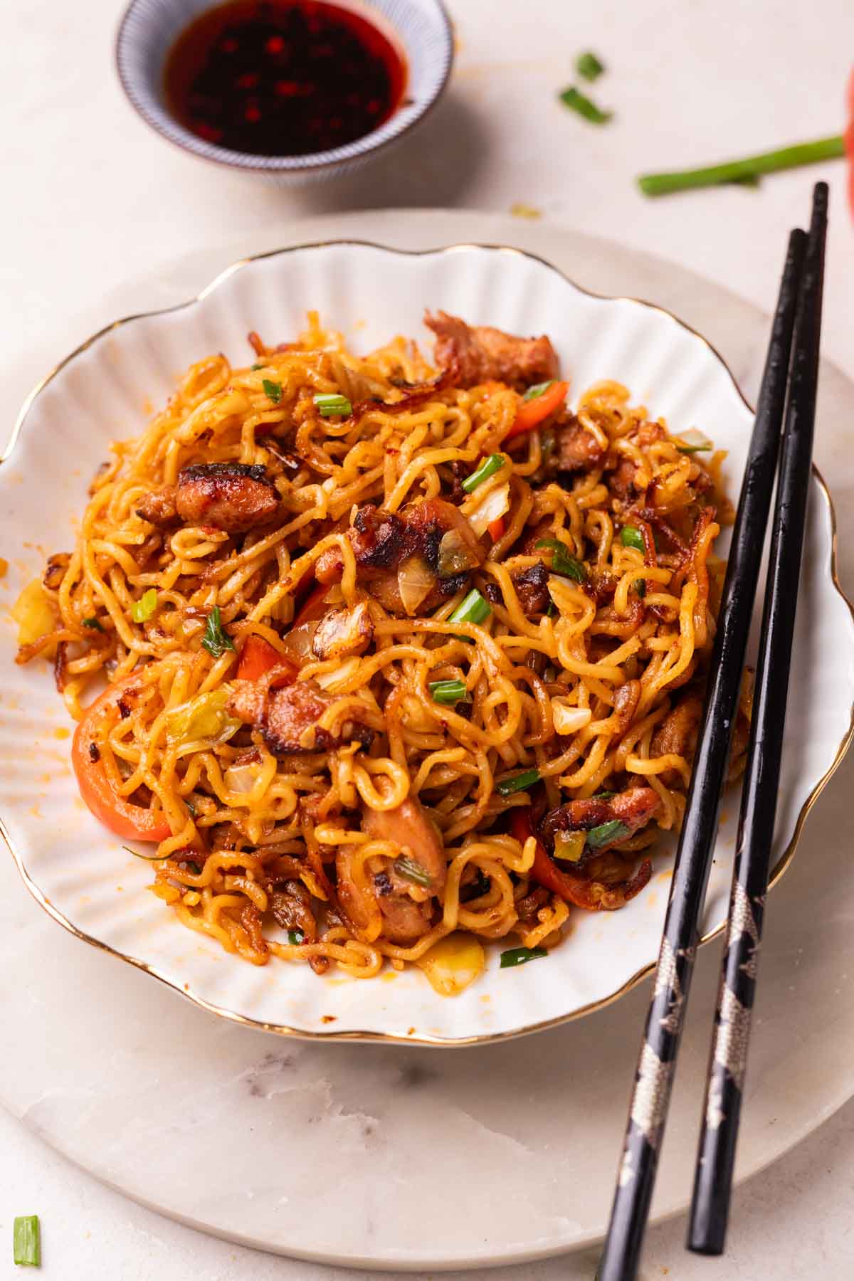 chilli chicken noodles served in a white bowl with chopsticks and soy sauce