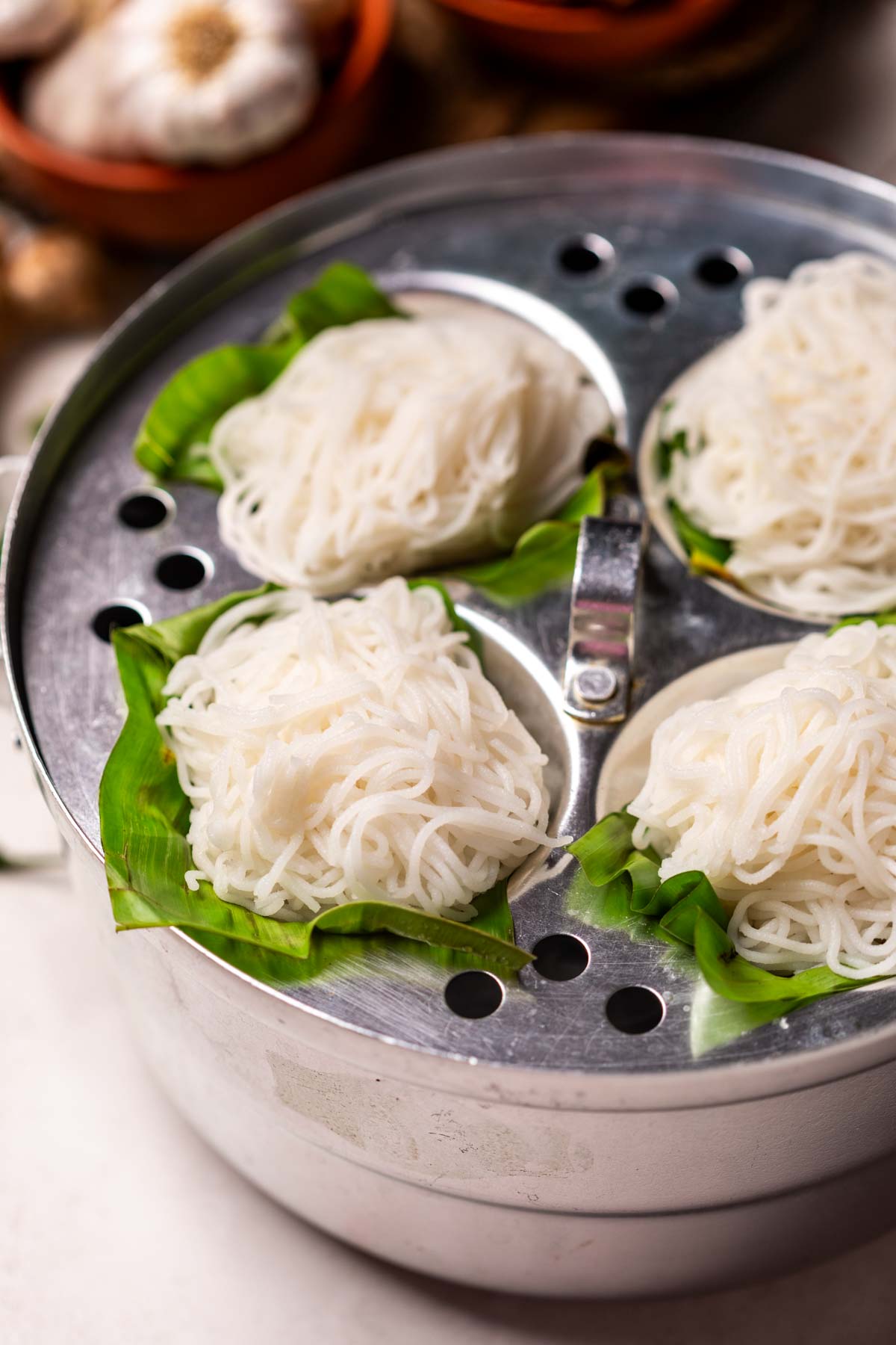 Rice Idiyappam pictured in a steamer over banana leaf