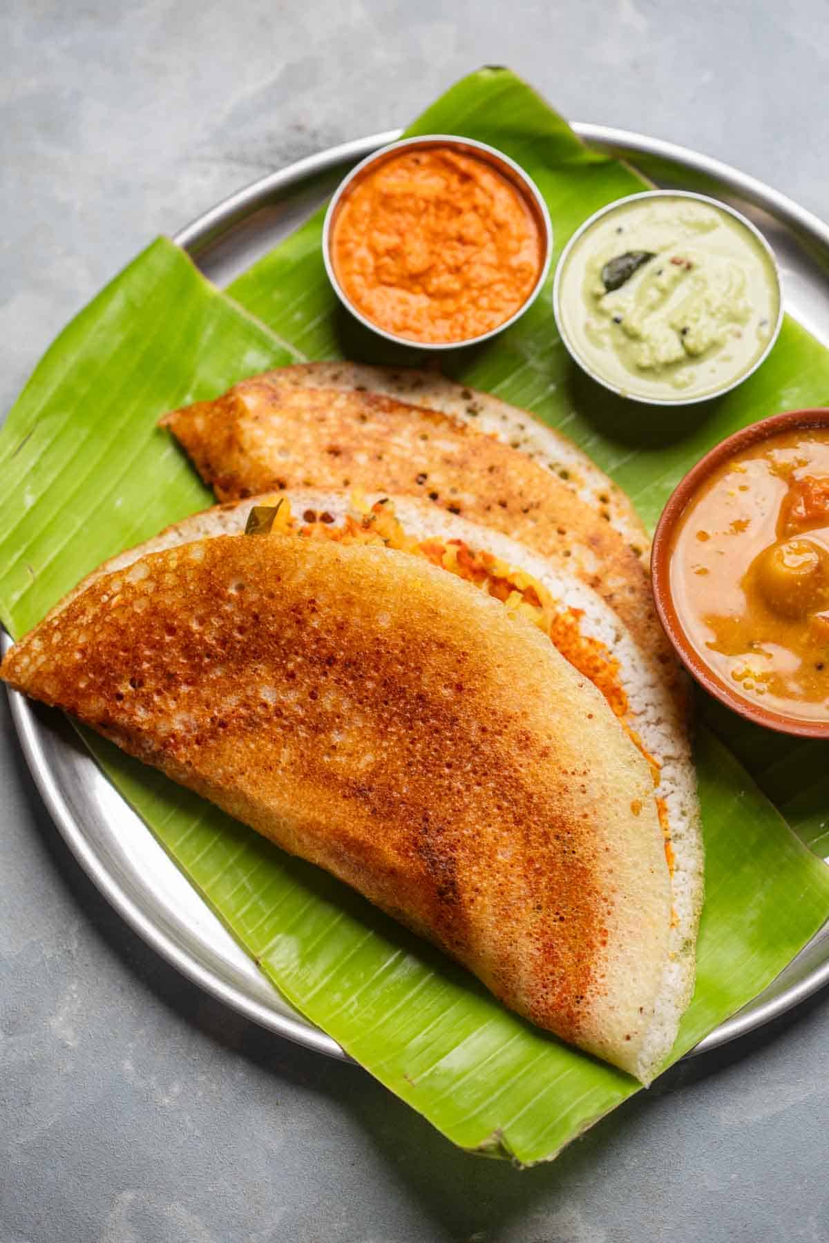 freshly made dosas served on a banana leaf platter with accompaniments
