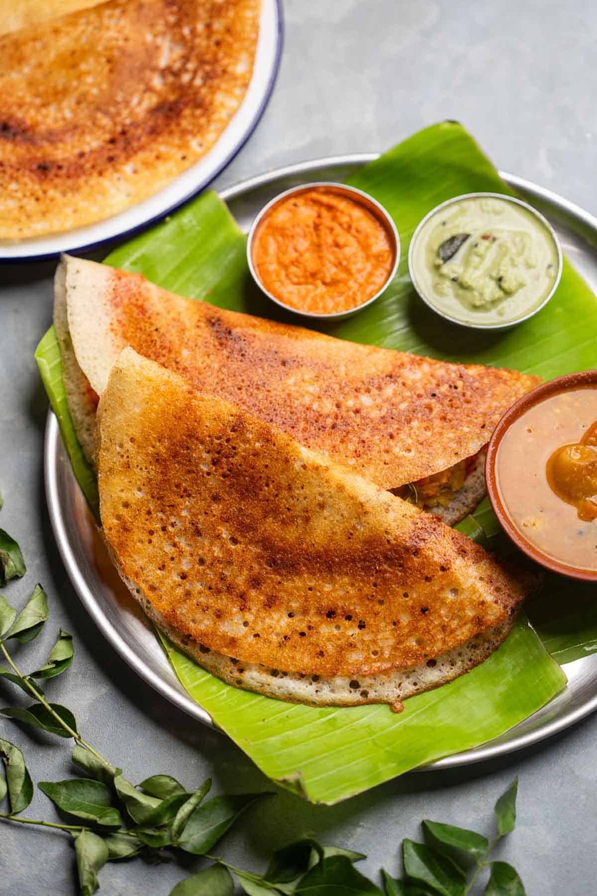 freshly made dosas served on a banana leaf platter with accompaniments