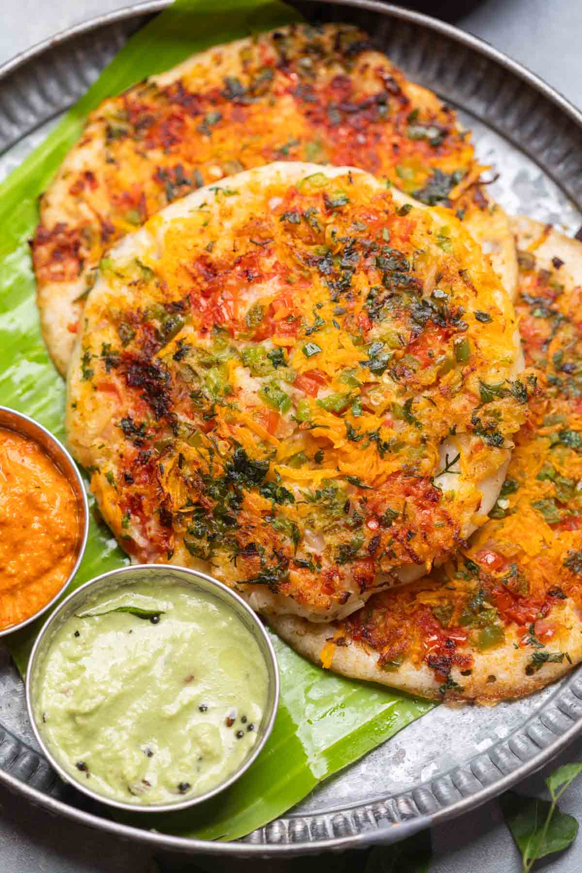 uttapams served with chutneys on a banana leaf platter