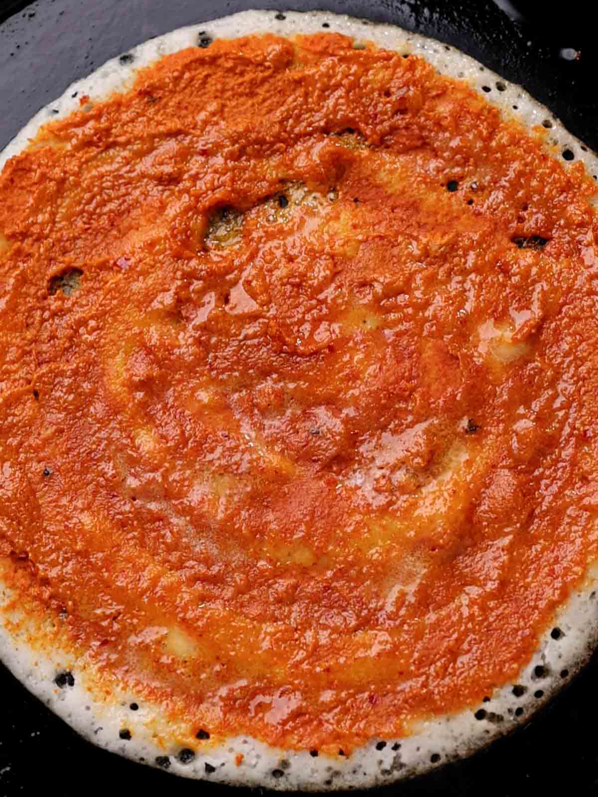 Red chutney spread on a mysore masala dosa on the pan