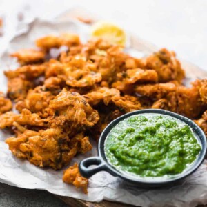 Crunchy vegetable pakoras served on a wooden board with green coriander chutney