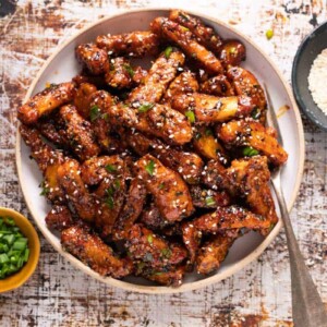 Honey chilli potatoes served on a white bowl with spring onions and sesame seeds on the side
