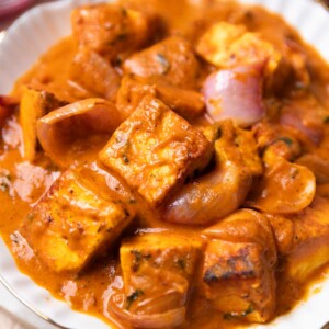 Paneer do pyaza served in a white bowl with accompaniments