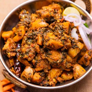 dhaba style aloo palak served in a bowl with sliced onions and a lemon wedge