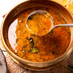 orange rasam in a container with a ladle