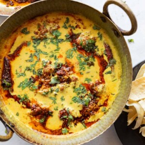 vibrant kadhi pakora garnished with a tadka and coriander leaves, served in a copper handi