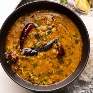 A bowl of Dhaba style Moong Dal served with rice and sliced onions on a plate
