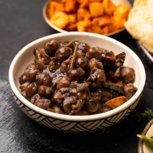 Bowl of pindi chole served with bhatura and potatoes on the side