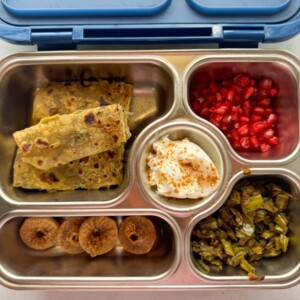Dal paratha served in a kids tiffin box with fruits, nuts, curd and veggies