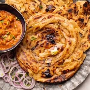 Lachha Parathas served on a plate with curry and onions