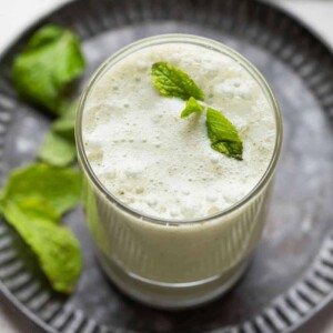 pudina chaas with ice cubes served in a glass on a metal tray