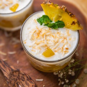 coconut pudding with pineapple jelly garnished with toasted coconut flakes, pineapple slice and mint leaves and served in shot glasses