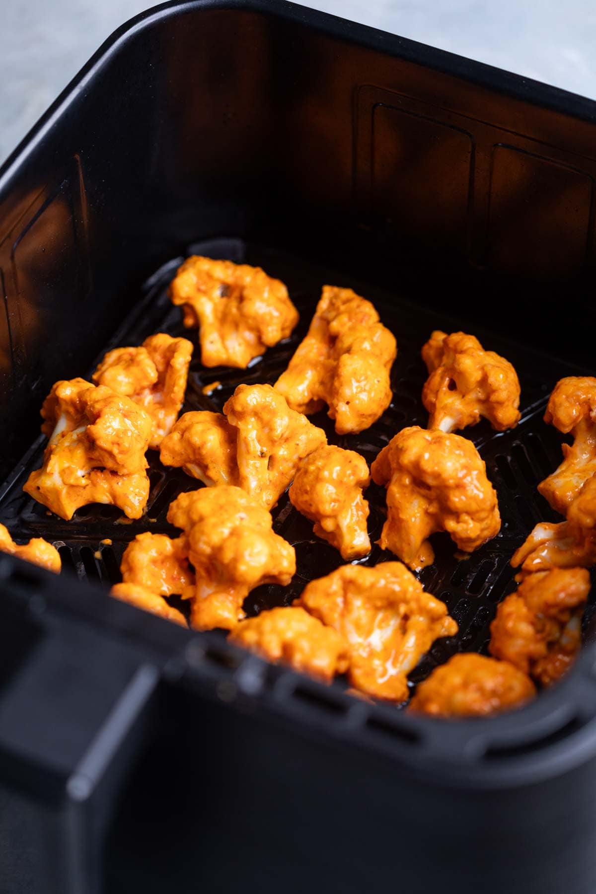 marinated bang bang cauliflower florets arranged in the air fryer basket ready to be cooked