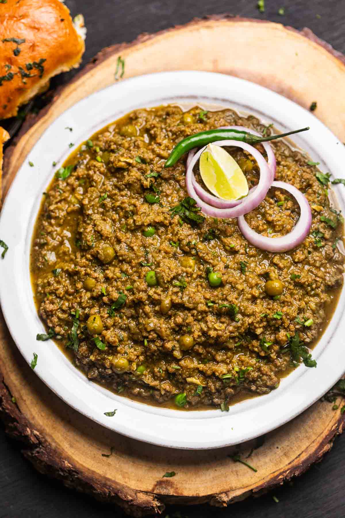 green keema masala served in a white bowl with onion rings, slit green chillies, and a lemon wedge