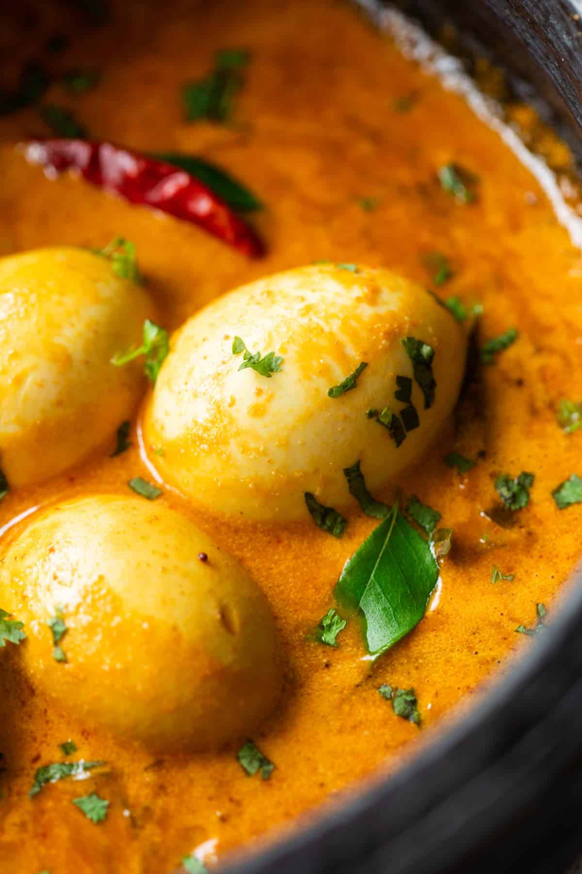 South Indian style Egg Curry is incredibly easy to make. A few spices, onions, tomatoes and coconut milk make this utterly satisfying and comforting egg curry recipe that tastes best with parathas (flatbread) and rice. Make extras because everyone will want seconds! #indian #curry #recipe #coconut #eggs close up image of south indian style egg curry to show the creamy texture and perfectly boiled eggs