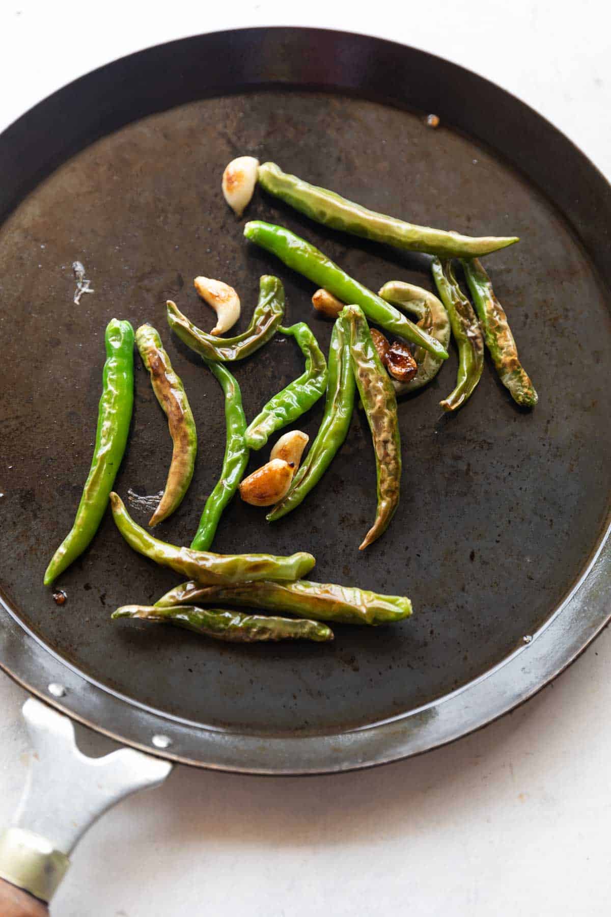 an image of blistered green chillies and garlic on a tawa to make thecha