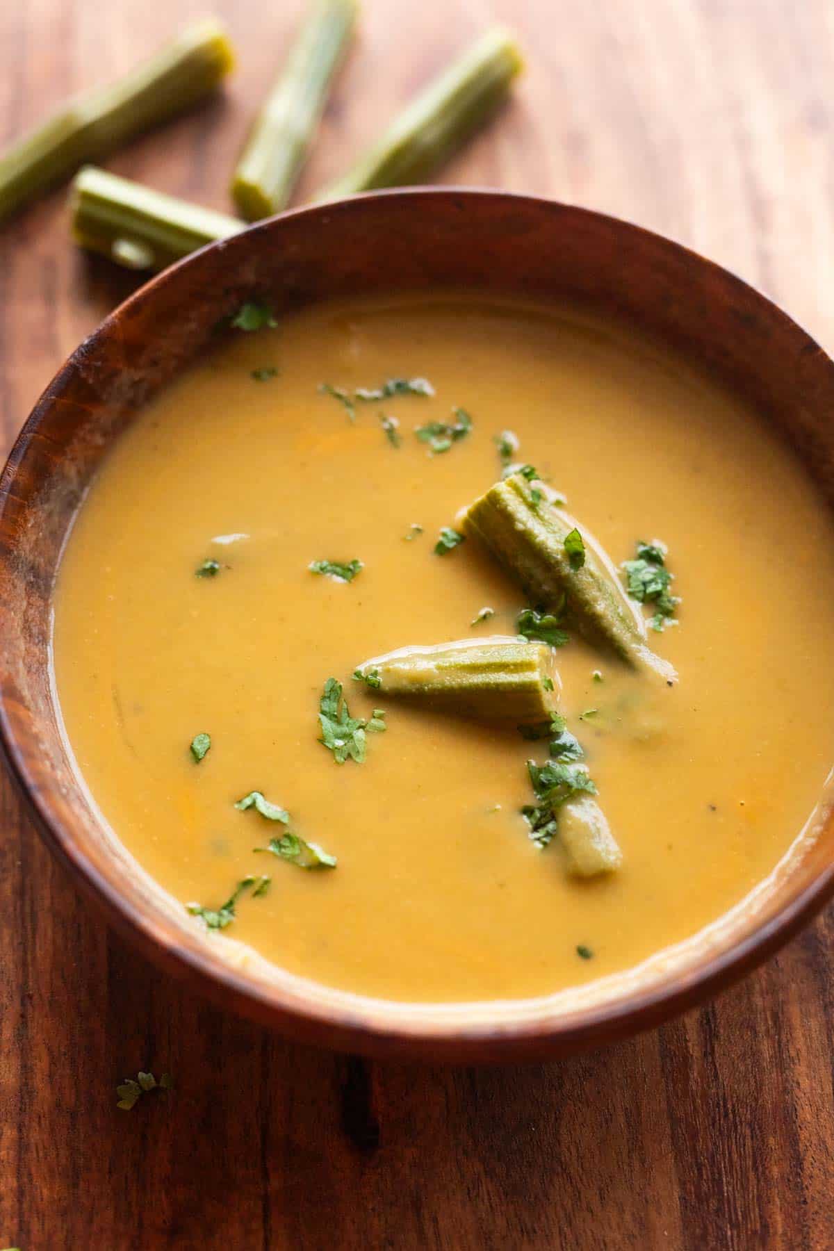 drumstick soup served in a wooden bowl and garnished with boiled drumsticks and coriander leaves