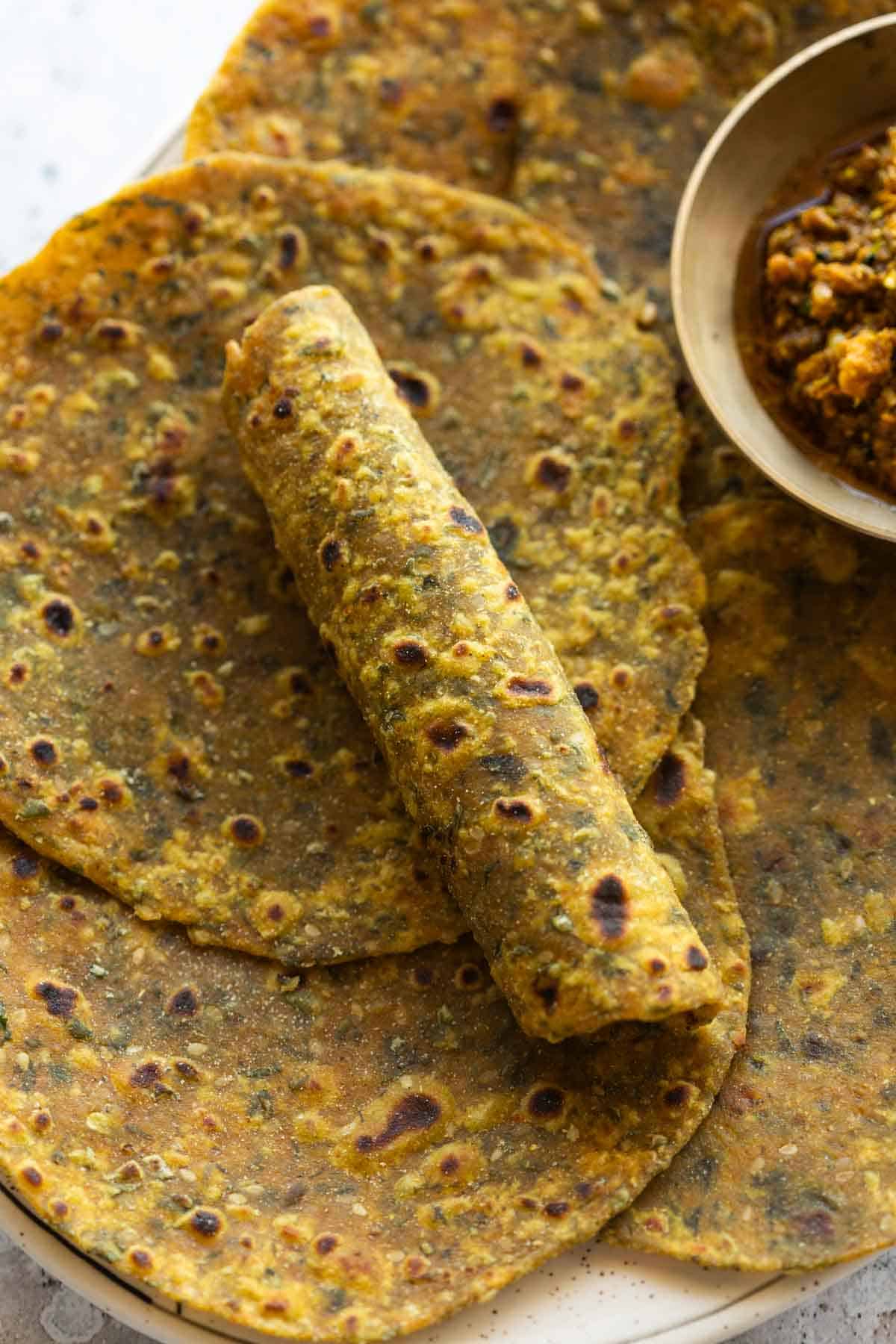 close up image of freshly made methi thepla with one rolled to showcase it's soft texture