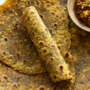 close up image of freshly made methi thepla with one rolled to showcase it's soft texture