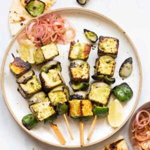 a shot of hariyali paneer tikka on skewers placed on a white plate