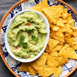Crazy good homemade guacamole served in a white bowl with chips on the side.