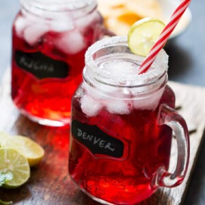 Cranberry Ginger Holiday Cocktail served in mason jars with sugar coated rims and a slice of lime. .