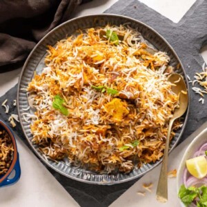 Paneer Biryani served on a grey plate with fried onions on the side