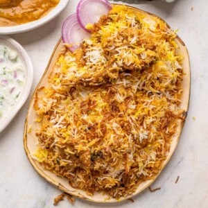 Mutton biryani served on a platter with sliced onions, raita and mirchi salan