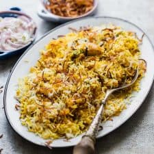 Chicken Biryani served on a platter with crispy fried onions and onion raita.