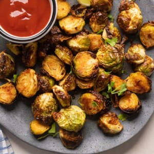 Roasted air fryer brussel sprouts served on a grey plate with ketchup on the side