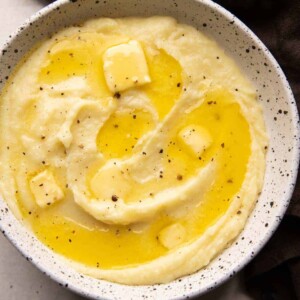 Mashed potatoes served in a white bowl with pools of butter on top