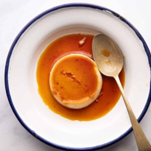Overhead picture of coconut caramel custard served on a white plate with a blue edging and a spoon