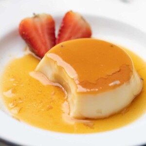caramel cusstard served on a white plate with strawberries on the side.