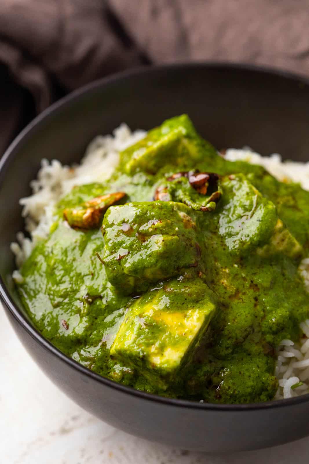 Palak paneer serve on top of jeera rice in a black bowl