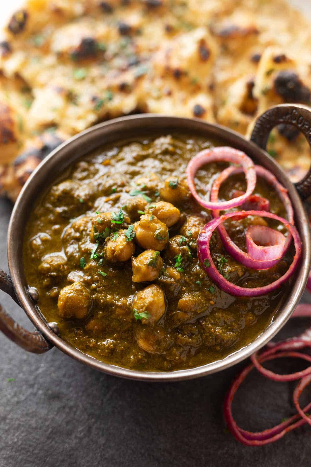 a bowl of chole palak served along with onion rounds and naan