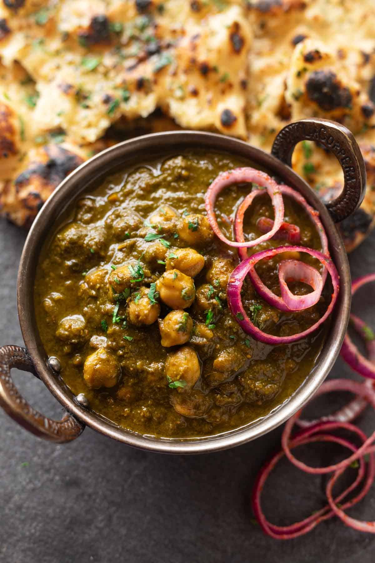 a bowl of chole palak served along with onion rounds and naan