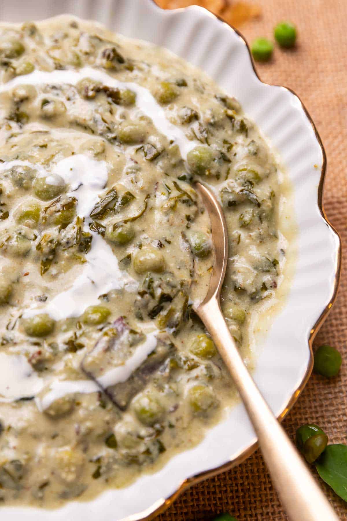 Close up of a spoonful of methi matar malai being taken out of a bowl