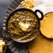 Picture of sarson ka saag served in a small copper kadhai with makki roti on the side