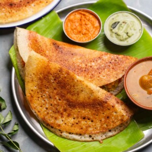 freshly made dosas served on a banana leaf platter with accompaniments