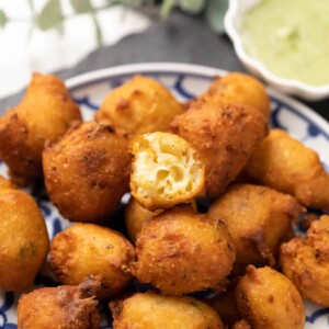 mysore curd bonda served on a white and blue plate with one bonda cut open
