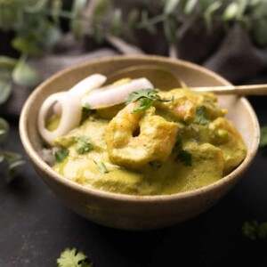 a bowl with white rice topped with green prawn curry with roundels of o