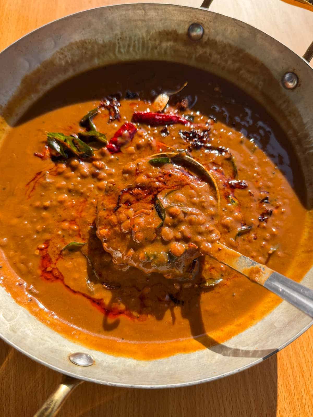 freshly made horsegram dal scooped up in a ladle to showcase it's color and texture