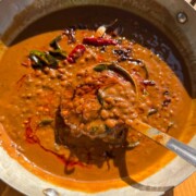 freshly made horsegram dal scooped up in a ladle to showcase it's color and texture