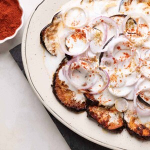 platter with fried eggplant slices and sliced onion topped with a curd mix