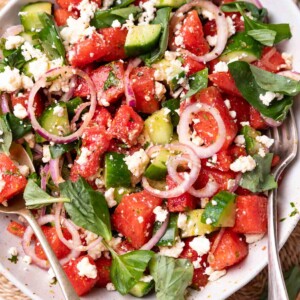watermelon salad in a white bowl with fork and spoon
