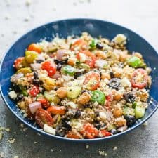 Mediterranean quinoa salad served in a blue bowl sprinkled with crumbled feta.